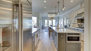 Una cocina moderna con electrodomésticos de acero inoxidable, una isla central, iluminación colgante y ventanas amplias.