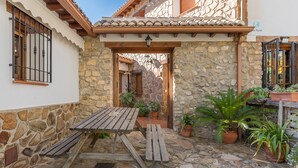 Un cortile con pareti in pietra, un tavolo di legno e panche, piante in vaso e un tetto in tegole.