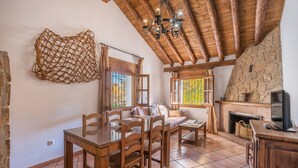Un ambiente rustico con un tavolo da pranzo in legno, sedie, un camino in pietra e un soffitto in legno.