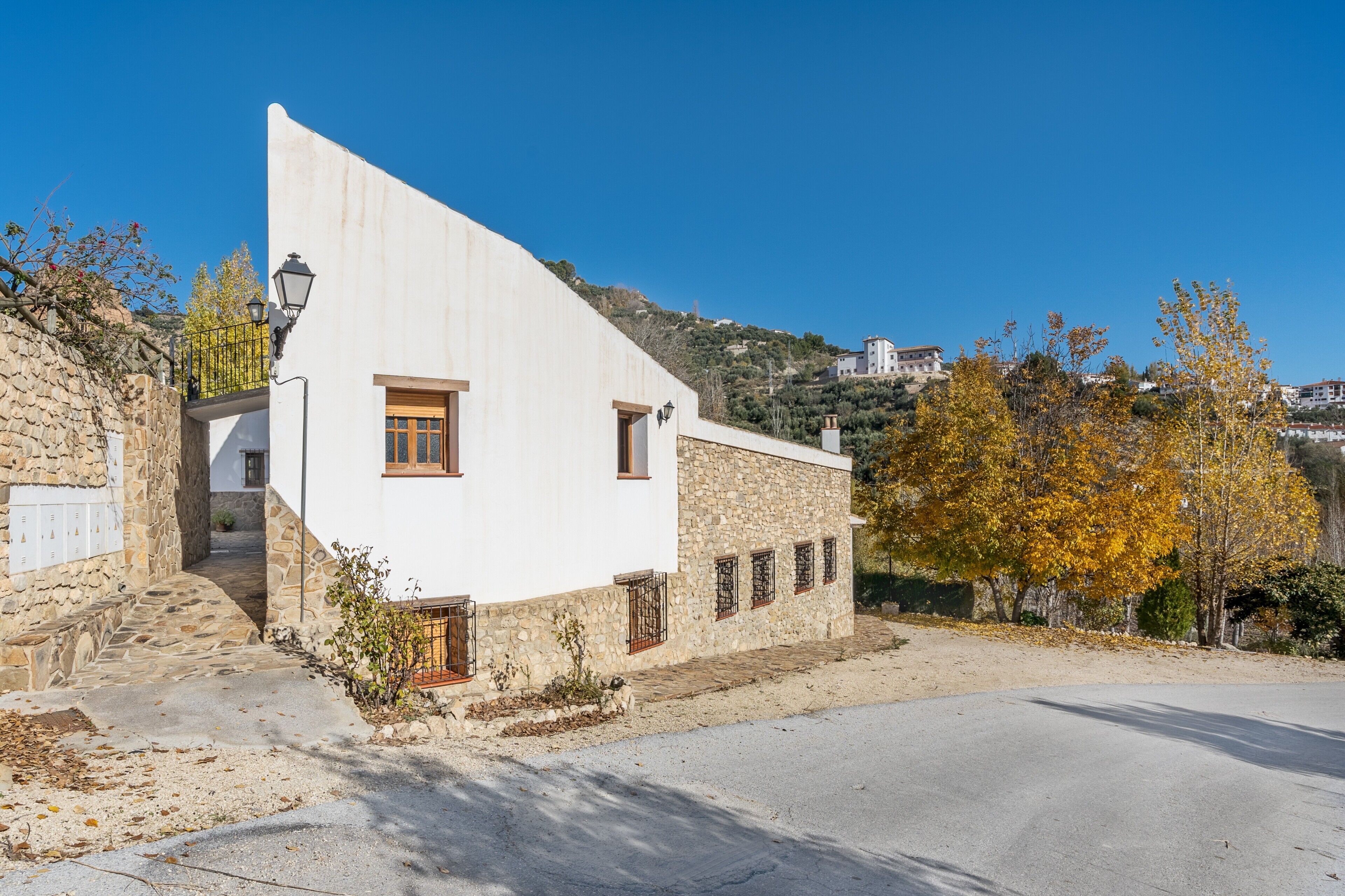 Un edificio blanco con base de piedra, una escalera y vistas a una colina con casas.