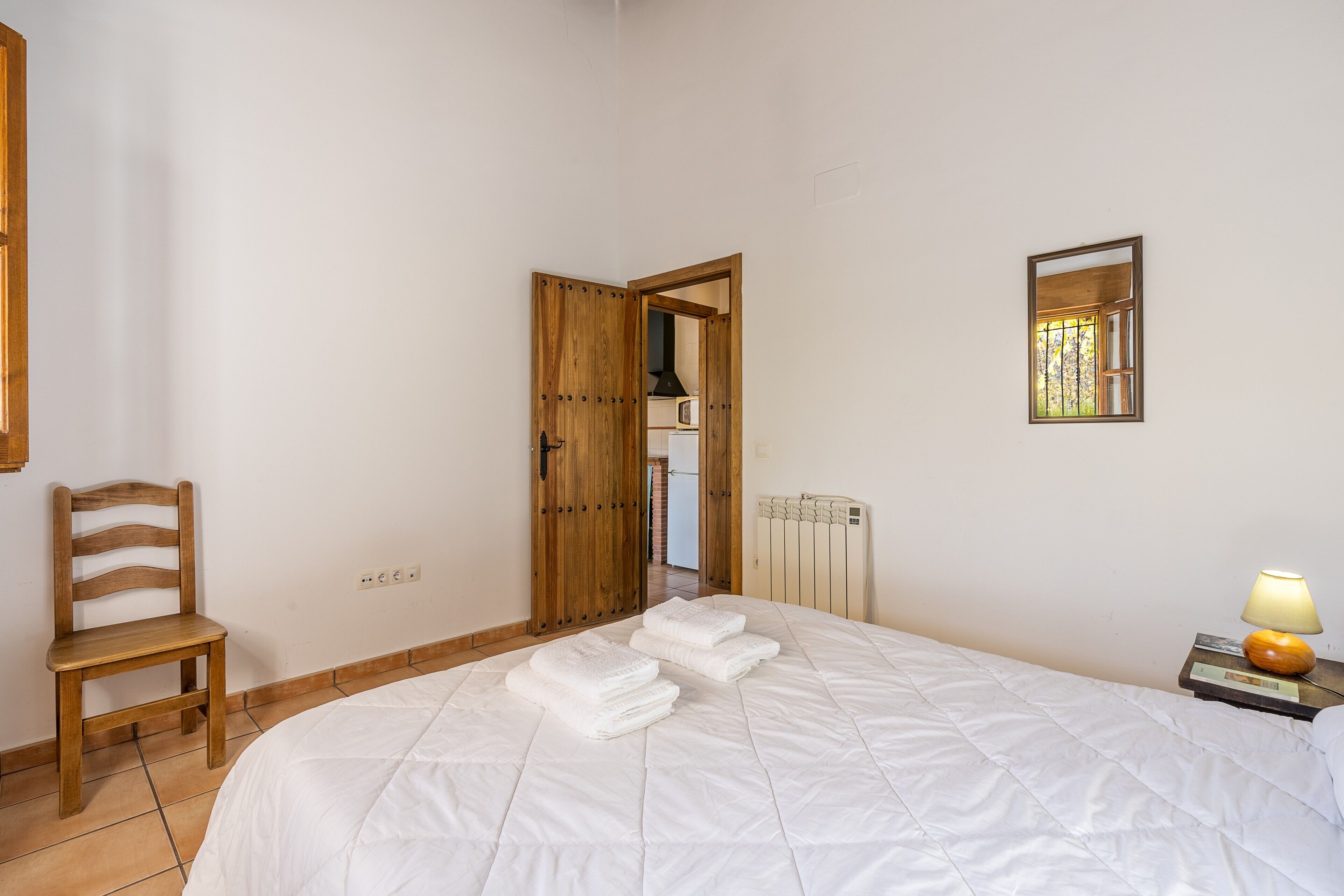 A bedroom with a bed, a chair, a radiator, a lamp, and a mirror.