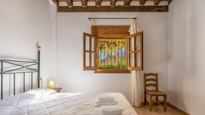 Une chambre à coucher avec un lit, une fenêtre avec des rideaux, une chaise et une table de chevet avec une lampe.