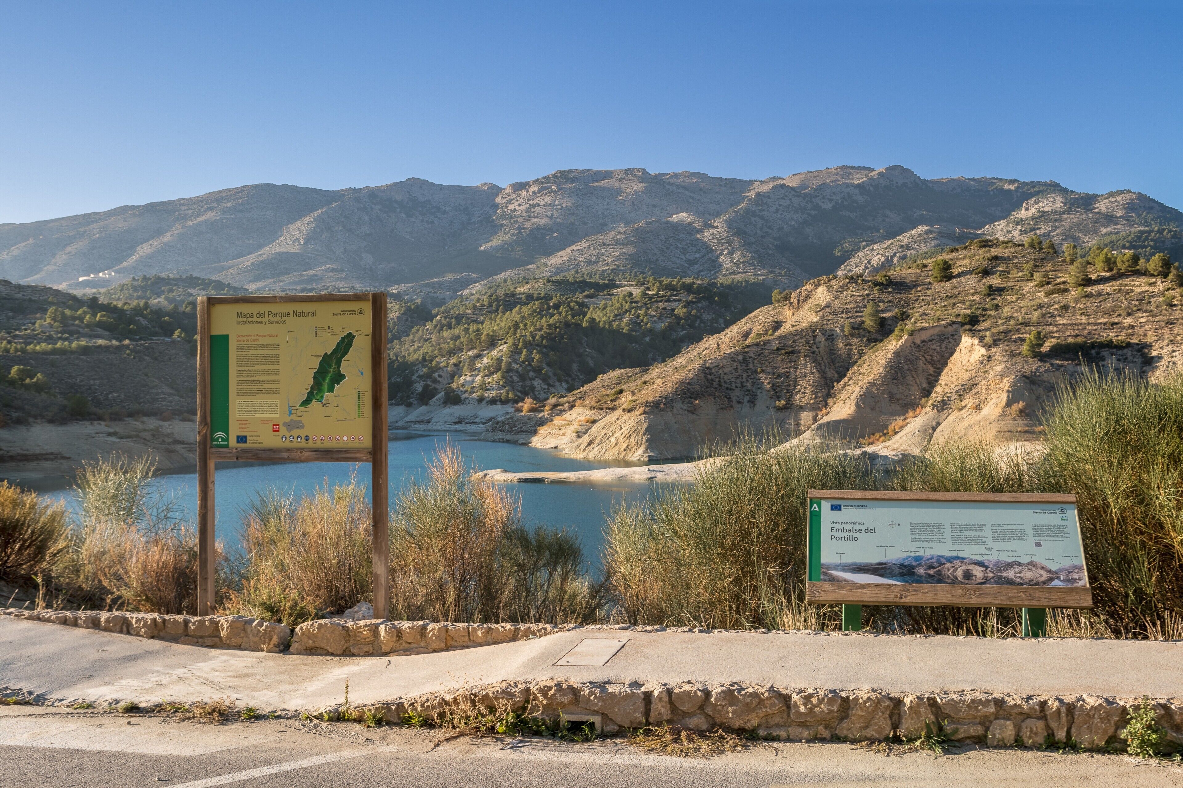 Un parco naturale con cartelli informativi, una strada e un paesaggio montuoso.