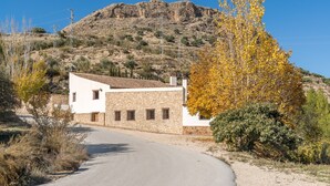 Un edificio de piedra con fachada blanca, un camino curvo y montañas al fondo.
