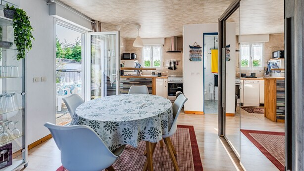 Une cuisine moderne avec un coin repas, une porte vitrée donnant sur l’extérieur et une vue sur le jardin.
