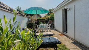 Une terrasse avec des meubles d’extérieur, un parasol vert et un bâtiment blanc doté d’une porte et d’une fenêtre.