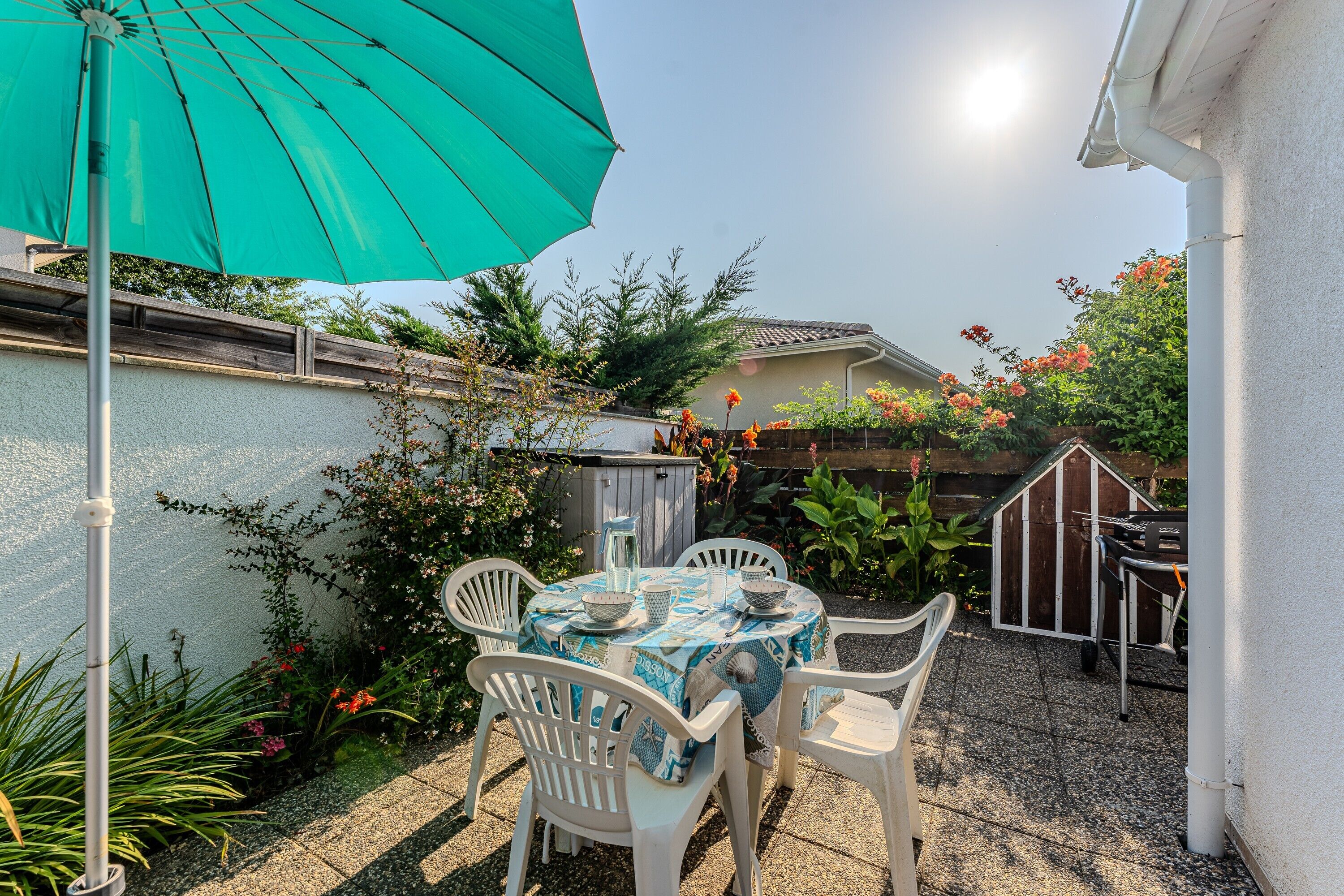 A patio with a table and chairs, a green umbrella, and a small shed.