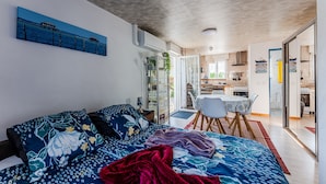 Une chambre à coucher moderne avec un lit, un canapé, un coin repas et une cuisine en arrière-plan.