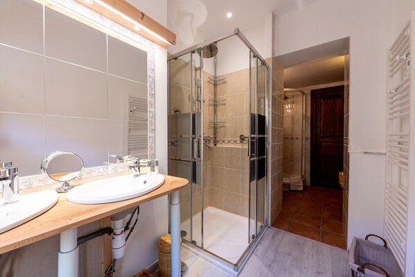 Un baño con ducha de vidrio, tocador de madera con dos lavamanos y un espejo grande.