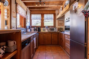 A kitchen with wooden cabinets, a stainless steel refrigerator, and a window with a view of the outdoors.