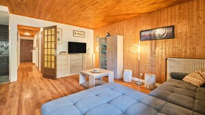 Una sala de estar acogedora con sofá, televisión, paredes de madera y una zona de cocina.