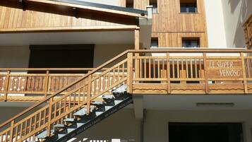 Un escalier en bois avec une rampe, menant à un bâtiment doté de nombreuses fenêtres et d’une enseigne sur laquelle on peut lire « LE SUPER VENOSC ».