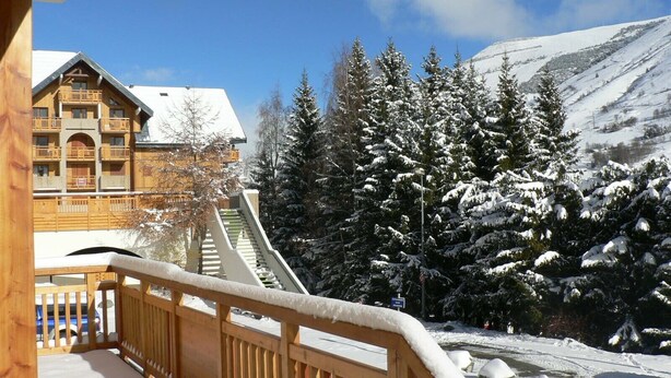 Un balcón de madera con vistas a una montaña nevada y un edificio con balcones.