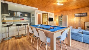 Una mesa de billar en una sala con techo de madera, zona de bar y un sofá.