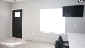 A room with a black door, a ceiling fan, a large window, a flat-screen TV, and a dining table with chairs. - Charming 1-bedroom house with WiFi, AC in peaceful Santa Clarita Brand New (Santa Clarita)