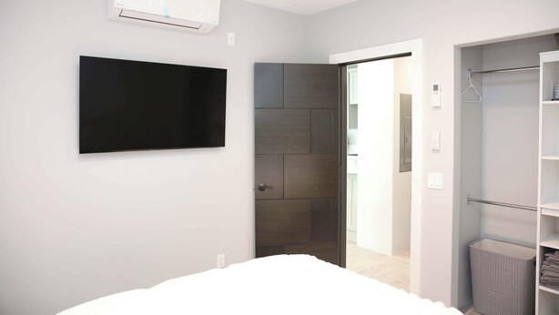 A modern bedroom with a bed, a flat-screen TV, an air conditioning unit, a wardrobe, and a door leading to another room. - Charming 1-bedroom house with WiFi, AC in peaceful Santa Clarita Brand New (Santa Clarita)