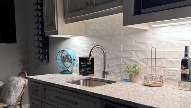 A modern kitchen with grey cabinets, a stainless steel sink, a blue fan, and a potted plant.