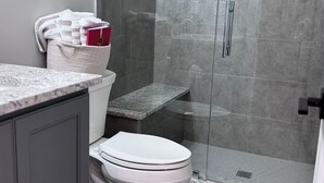 A modern bathroom with a toilet, shower, and a small shelf with toiletries.