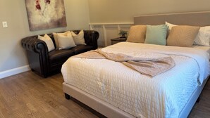A bedroom with a large bed, a dark leather sofa, and a wall-mounted abstract painting.