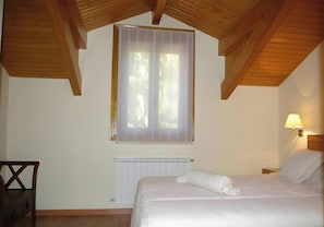 A bedroom with a wooden ceiling, a bed with white bedding, a window with sheer curtains, a wall-mounted lamp, and a radiator. - Apartment 'Casa Requias 1' with Lake View, Shared Garden and Wi-Fi (Requiás)