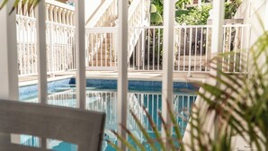 A pool area with a white fence, steps leading to a deck, and potted plants.