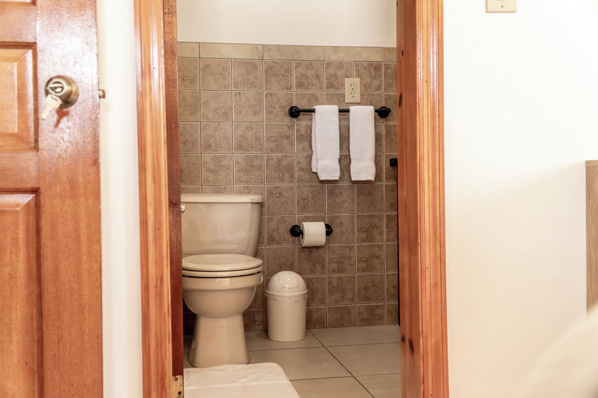 Un baño con inodoro, un bote de basura y un toallero con dos toallas.