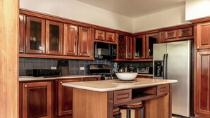 A kitchen with wooden cabinets, a stainless steel refrigerator, a microwave, and a large island with stools.