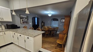 A kitchen with white cabinets, a granite countertop, and a dining area with wooden chairs and a table. - Charming 2-bedroom bungalow with WiFi and AC in serene Mount Carmel (Mount Carmel)