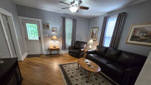 A living room with a ceiling fan, two leather sofas, a coffee table, and a patterned rug. - Charming 2-bedroom bungalow with WiFi and AC in serene Mount Carmel (Mount Carmel)