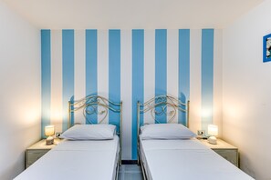 A room with two beds, a striped wall, and bedside lamps.