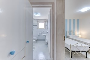 A hotel room with a bed, a bathroom with a toilet and sink, and a hallway leading to another room.