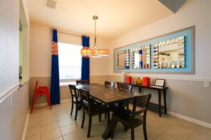 Un comedor con una mesa de madera, sillas, un taburete rojo, una lámpara de techo y un espejo grande en la pared.