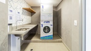 Une petite buanderie équipée d’un lave-linge, d’un évier et d’une étagère en bois.