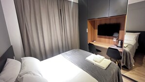 Une chambre d’hôtel moderne dotée d’un grand lit, d’un bureau avec une chaise, d’un téléviseur à écran plat et d’une armoire en bois.