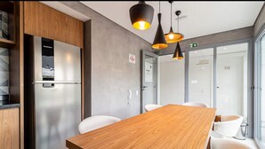 Une cuisine moderne avec un réfrigérateur en acier inoxydable, des armoires en bois, une table à manger en bois, des chaises blanches et des luminaires suspendus.
