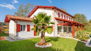 A two-story house with a red roof, white walls, and a palm tree in the front yard. - Villa Zeruko Izarra 5***** Wi-Fi & Air Conditioning, Mountain Views (Sare)