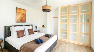 A bedroom with a bed, a wooden wardrobe, a hanging light fixture, and a painting on the wall.