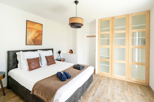 Un dormitorio con una cama, un armario de madera, una lámpara colgante y un cuadro en la pared.