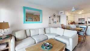 Een moderne woonkamer met een witte hoekbank, een houten salontafel en een keuken op de achtergrond.