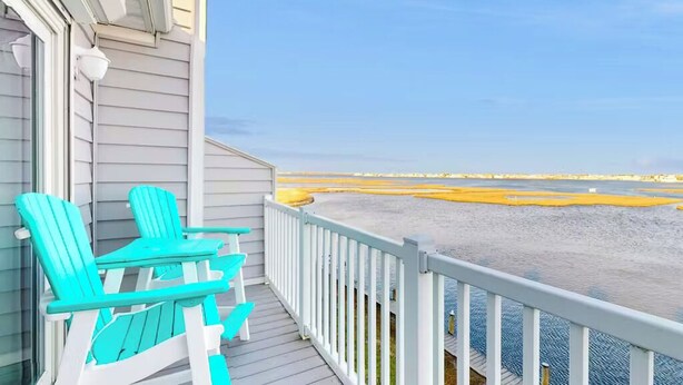 Een balkon met twee turquoise Adirondack-stoelen en uitzicht op een strand met geel zand.