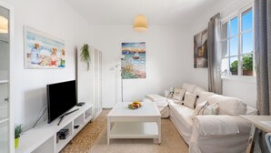 Een moderne woonkamer met een flatscreen televisie, een witte bank, een salontafel en kunstwerken aan de wanden.