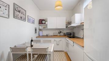 Una cocina compacta con armarios blancos, encimera de madera, lámpara colgante y comedor con mesa y sillas.