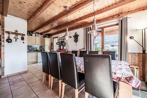 Un comedor con techo de madera, piso de baldosas y una mesa con sillas.