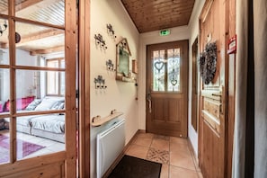 Un pasillo con paredes de madera, un radiador, una puerta con un panel de vidrio y una cama con almohadas.