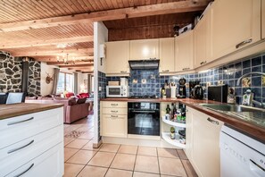A kitchen with wooden beams, a stone wall, a microwave, a stove, and a sink.
