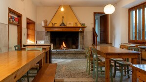 A cozy dining area with wooden tables and chairs, a fireplace, and a hanging light fixture. - Rifugio 'Camera Nel Verde' with Mountain Views, Shared Garden and Wi-Fi (Poppi)