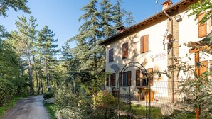 A rustic building with a gravel path leading to it, surrounded by dense trees. - Rifugio 'Camera Nel Verde' with Mountain Views, Shared Garden and Wi-Fi (Poppi)