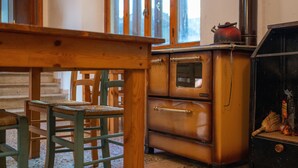 A room with a wooden table, green chairs, a vintage stove, and a window with a view. - Rifugio 'Camera Nel Verde' with Mountain Views, Shared Garden and Wi-Fi (Poppi)