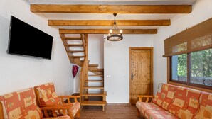 A room with a wooden staircase, a sofa set, a TV, and a window with a view.