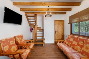 A room with a wooden staircase, a sofa set, a TV, and a window with a view.